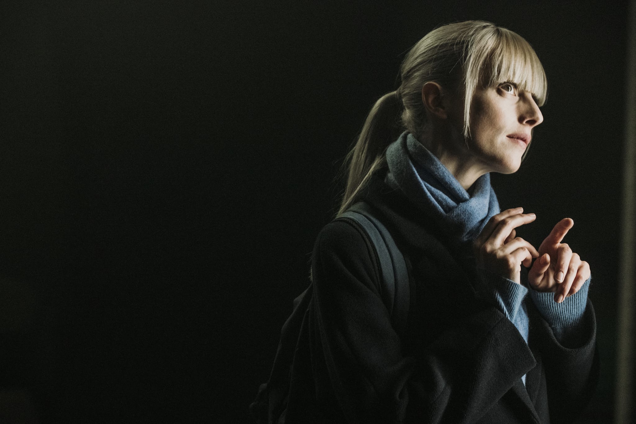 Astrid, a character from the TV mystery series Astrid & Raphaëlle. She's standing in shadows with sunlight on her face.